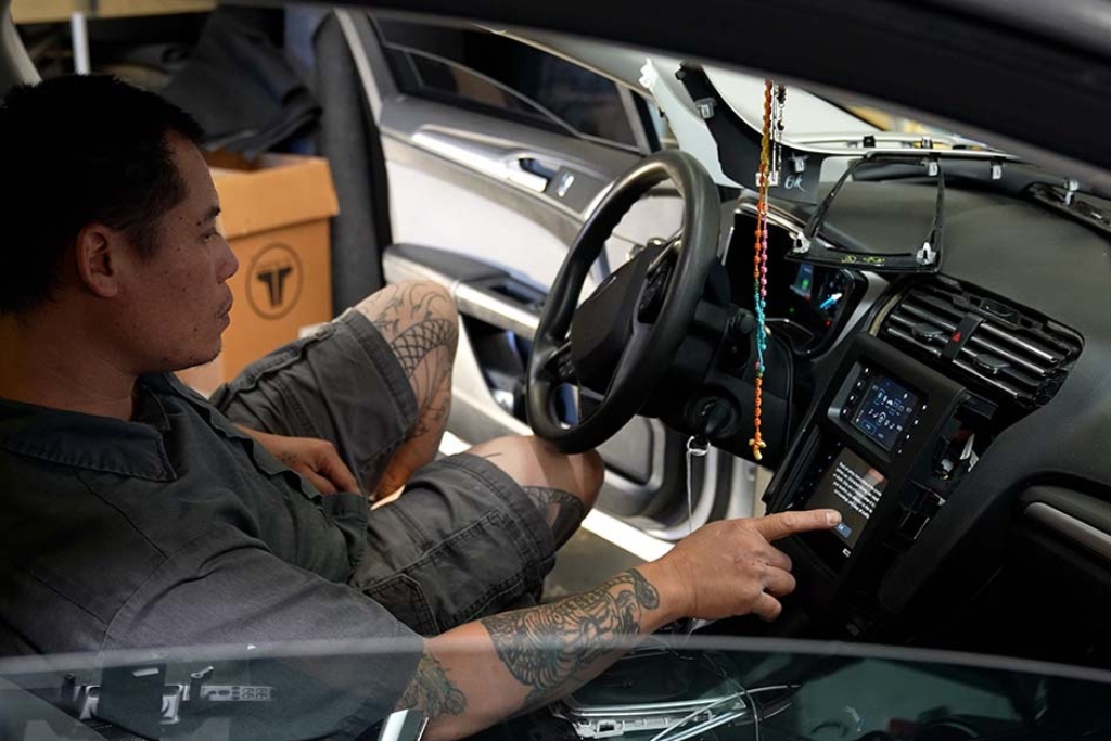 Technician seated inside a car while adjusting the touchscreen head unit during system tuning, part of the effort to optimize your system for fall travel.