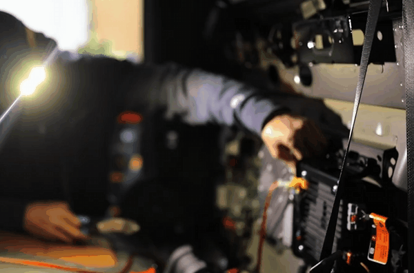 Close-up of a technician installing a car security system inside a vehicle door panel, with wires and modules visibly connected and illuminated by a bright work light. The technician's face is out of frame, emphasizing the detailed wiring work.