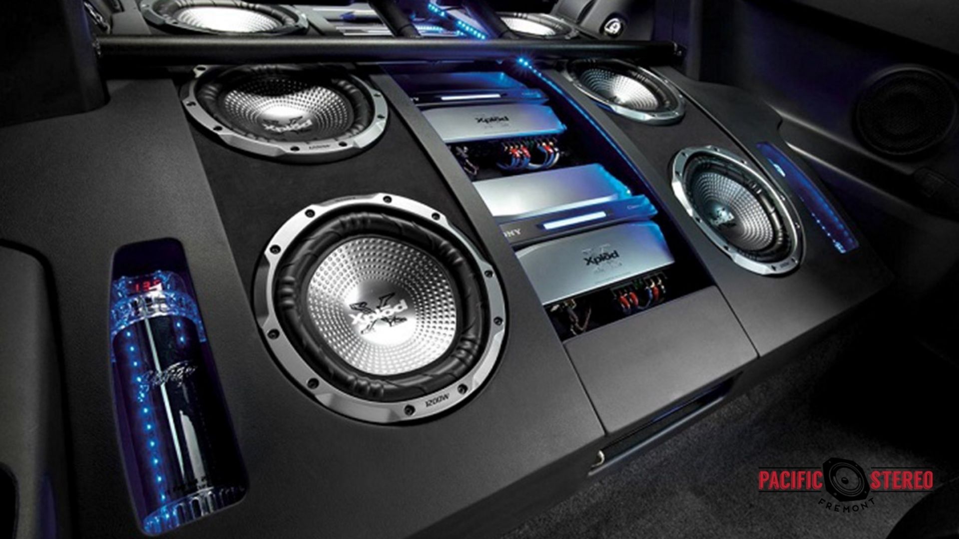 High-end custom car audio system installed in a vehicle trunk, featuring multiple Xplod subwoofers, amplifiers, and blue LED lighting.